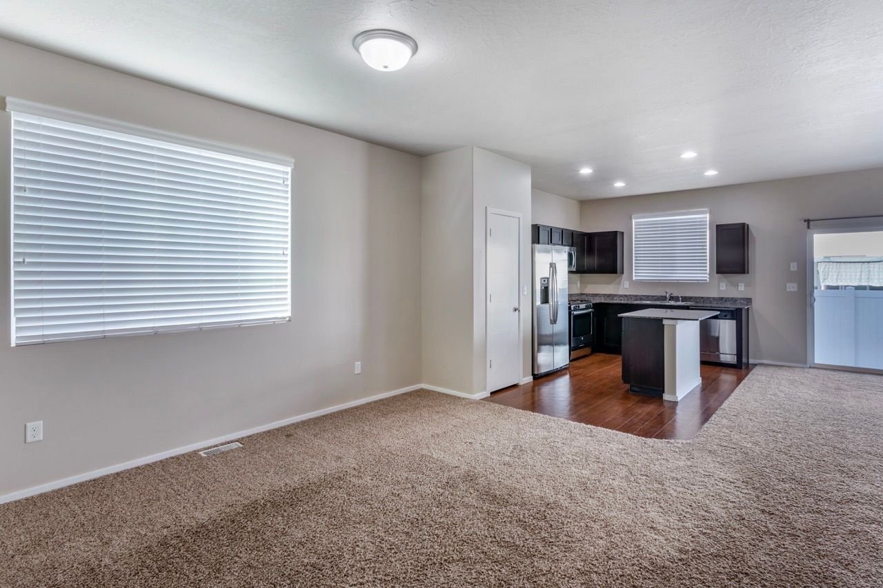 Open living area with beige carpet and a kitchen with dark cabinets, stainless appliances, and island.