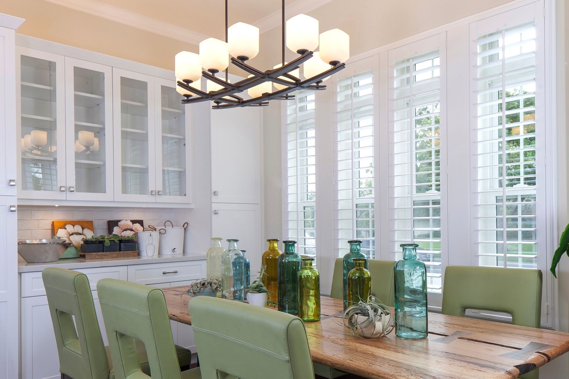 A living room with white shutters on the windows and a chandelier.
