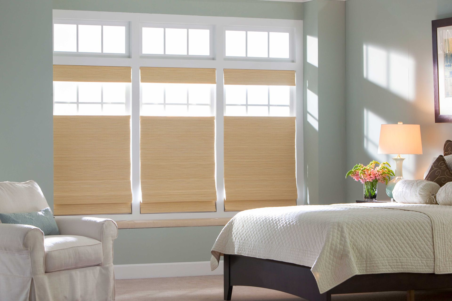 Bedroom with a window featuring light wood blinds, bed, armchair, and lamp on a bedside table.