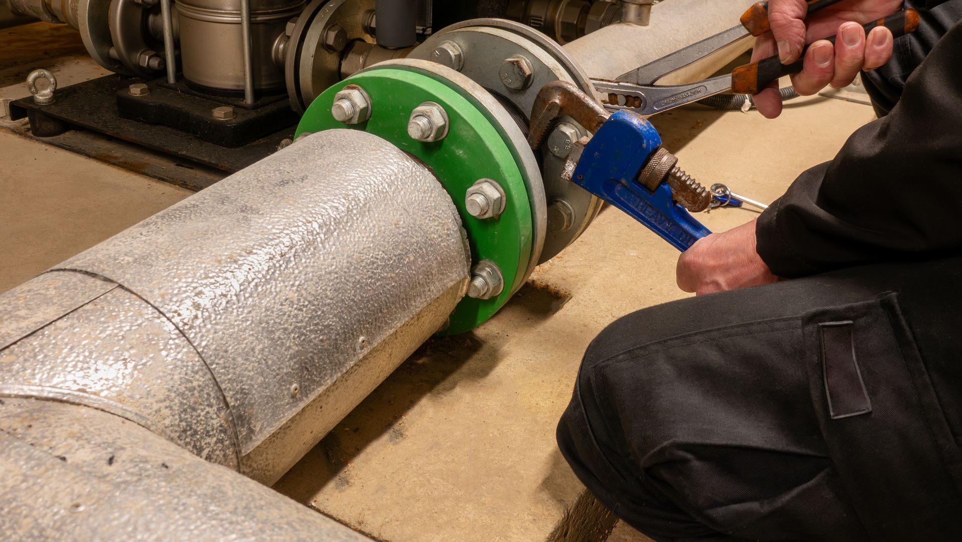 Technician tightening industrial pipe flange bolts with wrenches.