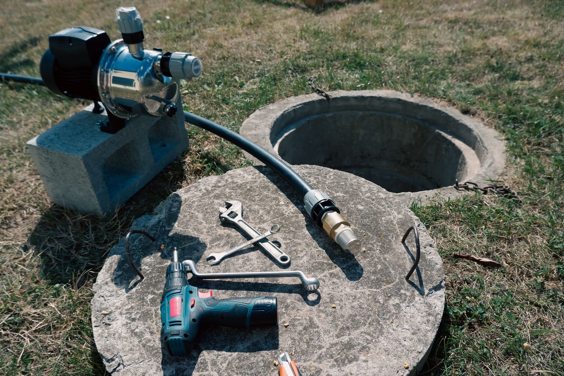 Well pump, tools, and hose positioned beside an open water well access.