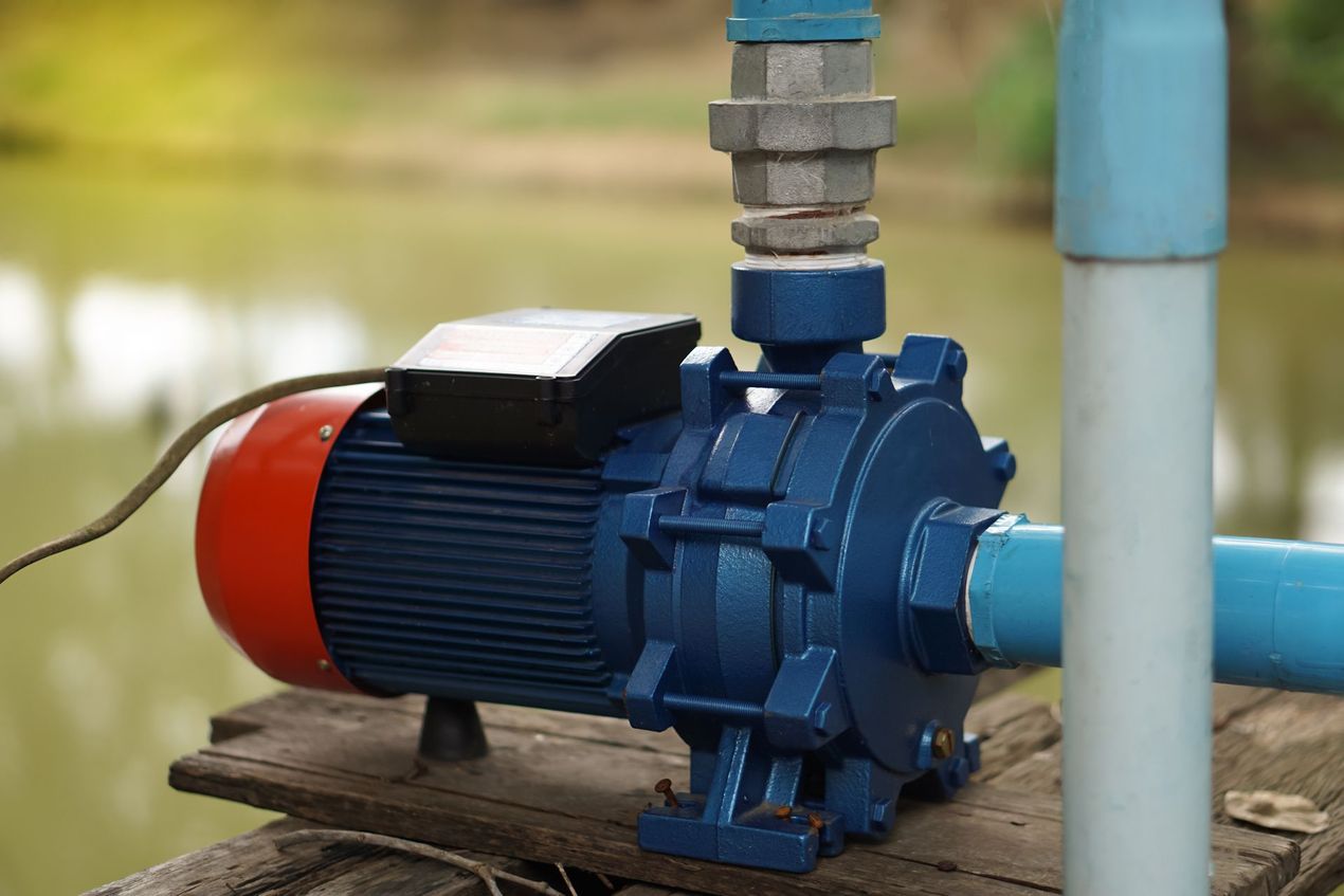 Blue water pump with red motor, piping, and electrical cord on a wooden platform near water.