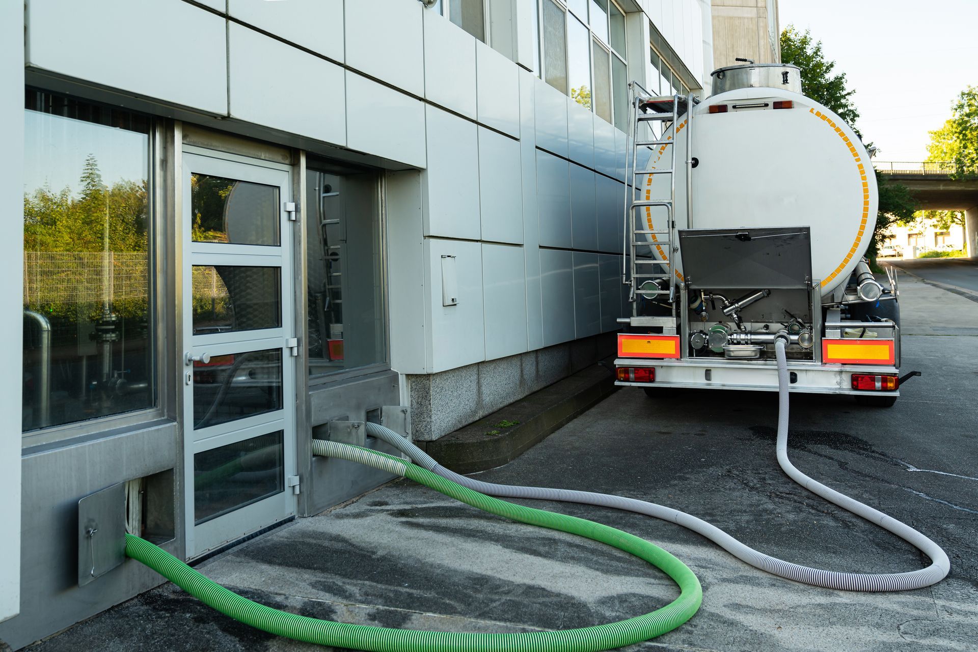 Vacuum tanker truck connected to a building with hoses for commercial pumping service. Vacuum tanker truck connected to a building with hoses for commercial pumping service.