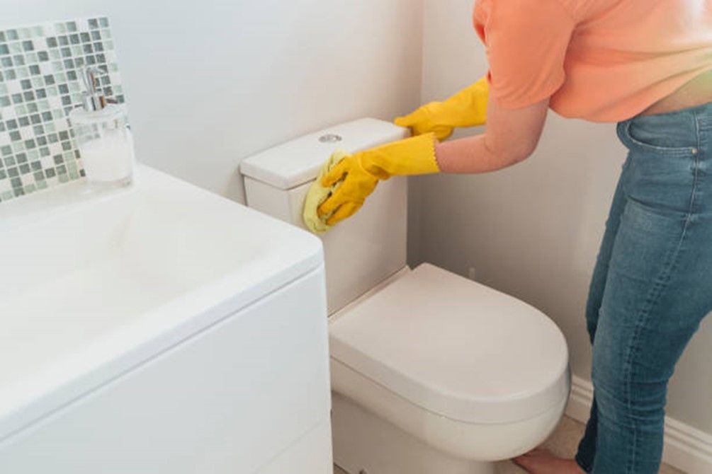 a woman in yellow gloves is cleaning a toilet in a bathroom .