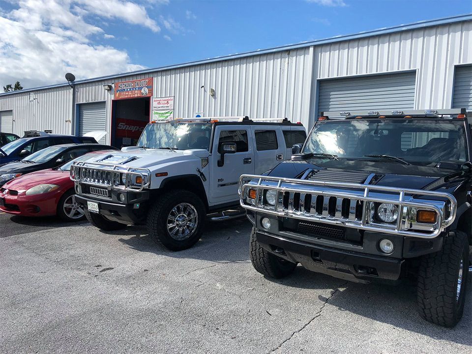 Three parked Hummer-style SUVs outside an auto shop on a cloudy day | Mechanic On Duty CB LLC