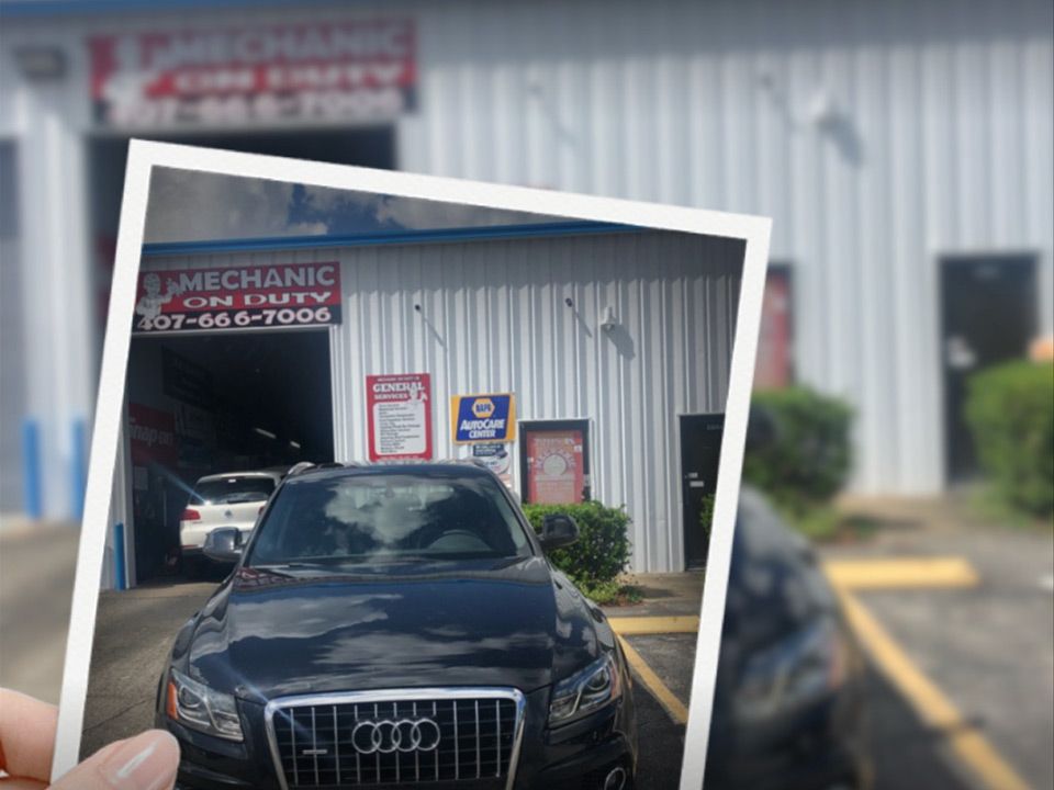 Black Audi parked outside a mechanic shop, shown in a printed photo held in front of the building | Mechanic On Duty CB LLC