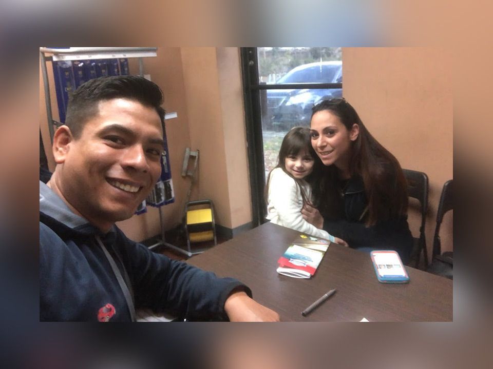 Three people sit at a table indoors, smiling for a selfie with a phone and small items on the table. | Mechanic On Duty CB LLC