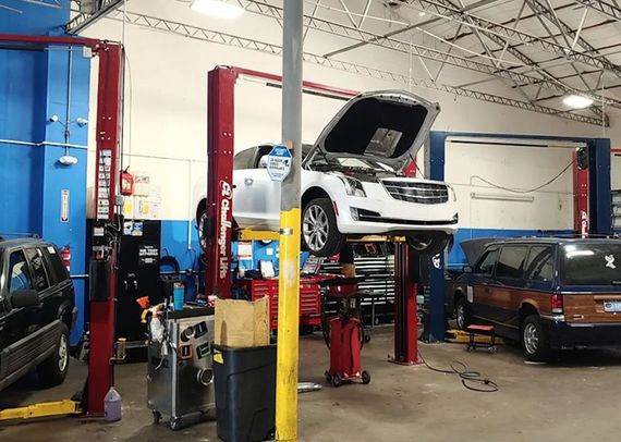 Auto repair shop with a white car raised on a lift, hood open, and other vehicles nearby | Mechanic On Duty CB LLC