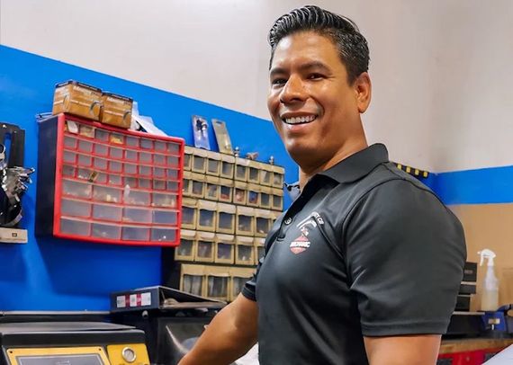 Smiling mechanic standing in a workshop beside organized parts bins and tools | Mechanic On Duty CB LLC