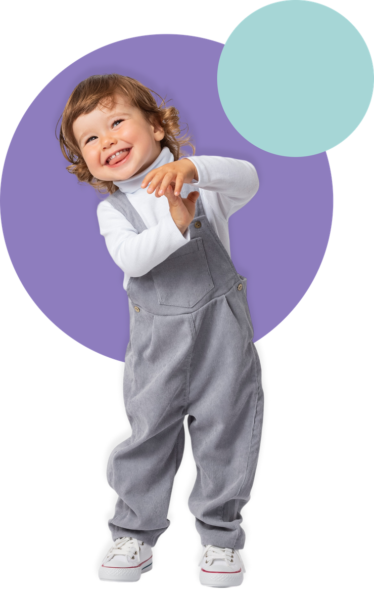 Smiling child in gray overalls and white shirt standing in front of purple and teal circles