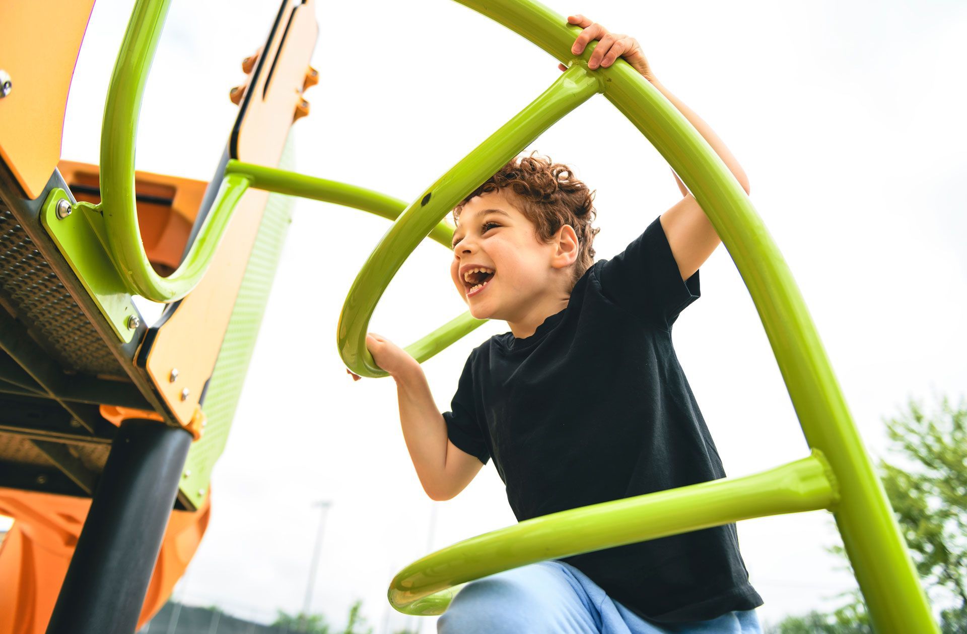 Child climbing bright green playground bars, smiling outdoors.