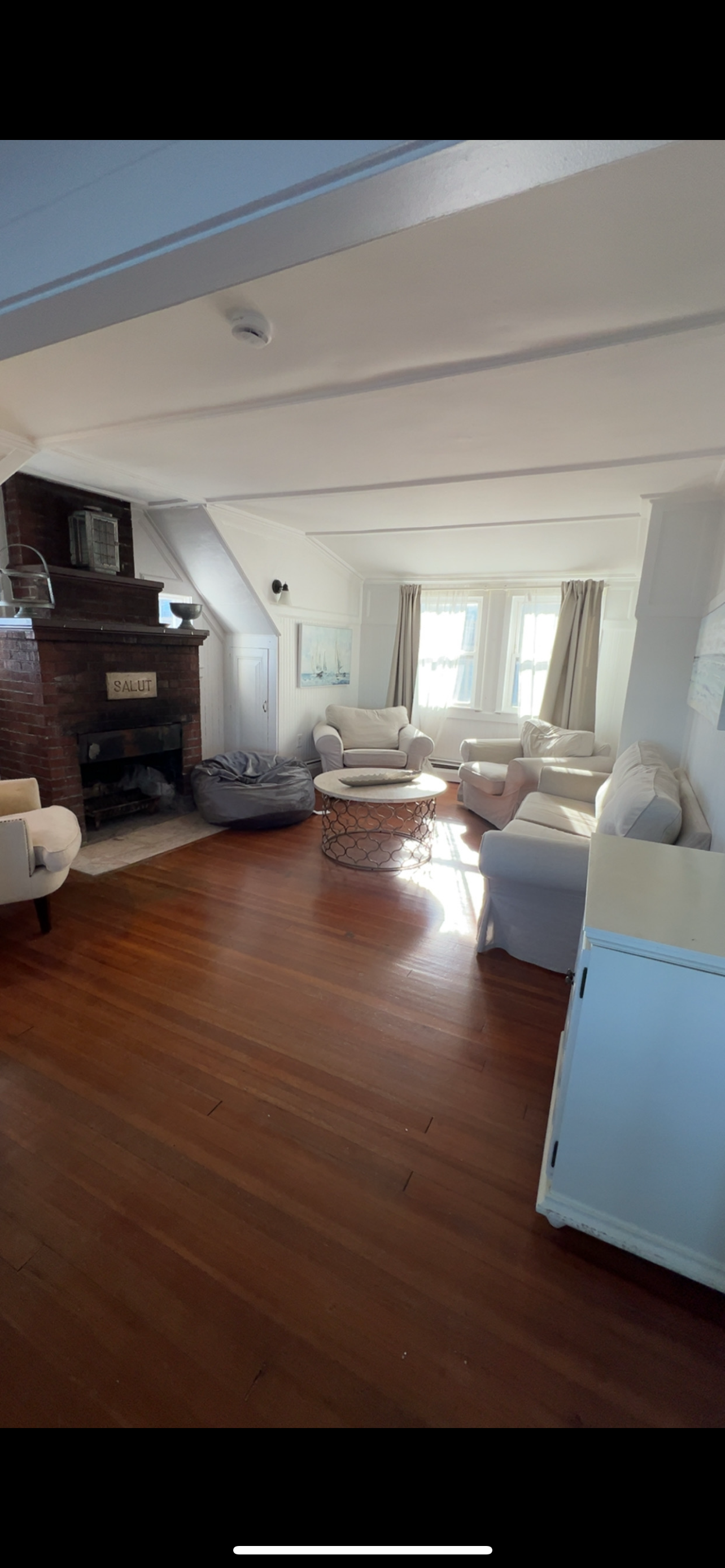 A living room with hardwood floors, a stone fireplace, and white furniture arranged around a round coffee table.