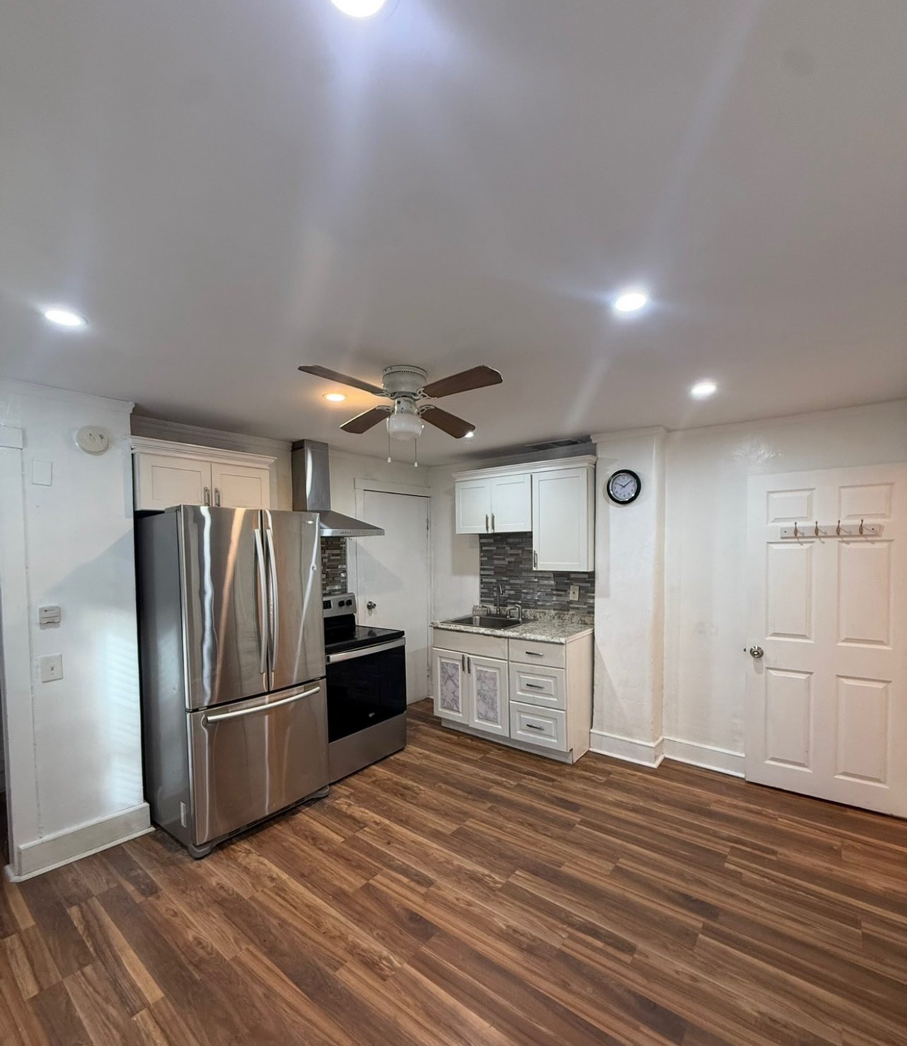 A small kitchen with wood floors, white cabinets, stainless steel appliances, and a central ceiling fan.