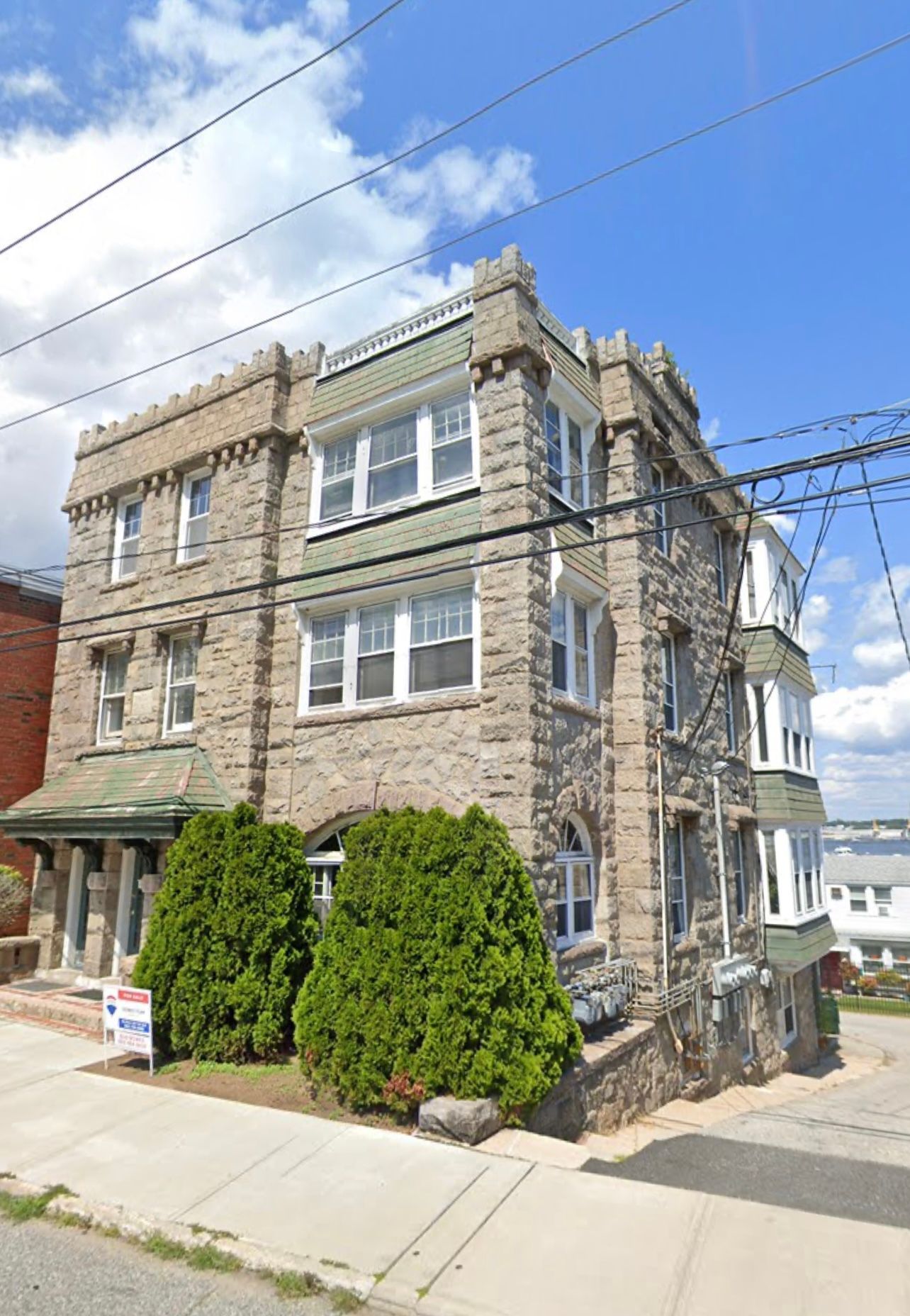 A three-story, stone apartment building with a crenelated roofline and a corner turret, under a bright blue sky.