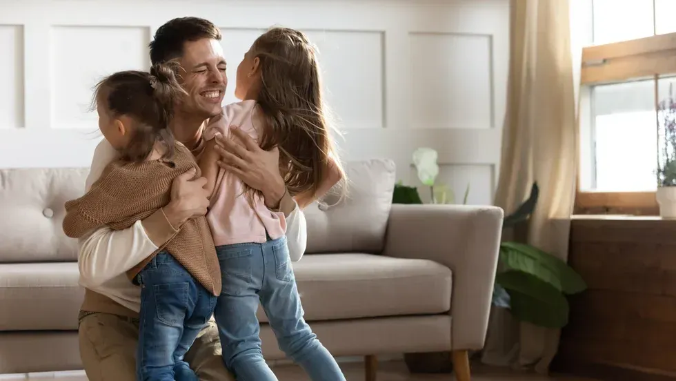 Two children hugging a smiling adult in a bright living room