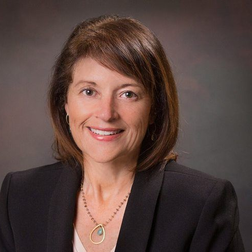 Studio portrait of a smiling woman in a black blazer and necklace on a gray background