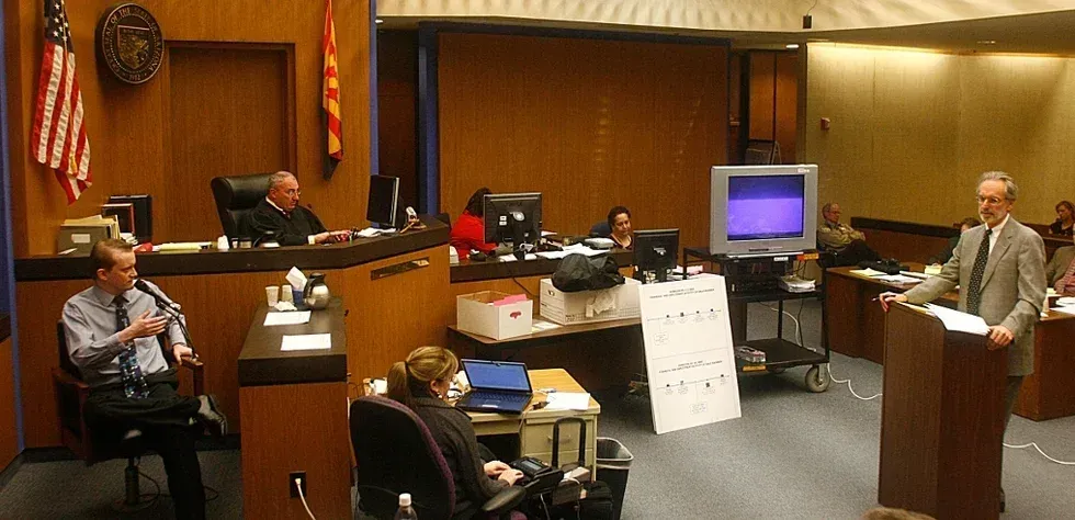 Council chamber with a man speaking at a podium while others sit at desks and monitors around the room.