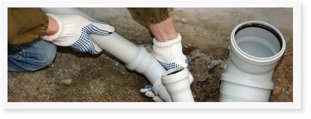 Een persoon met werkhandschoenen is bezig grijze pvc-buizen in de grond te installeren.