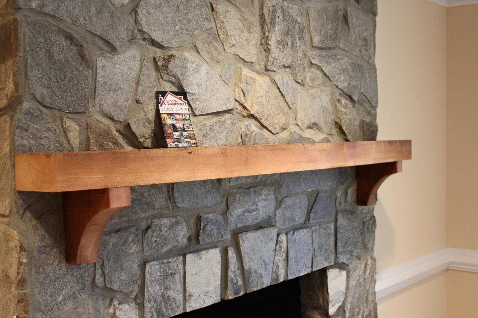 Stone fireplace with a wooden mantel and a small card on top in a living room.