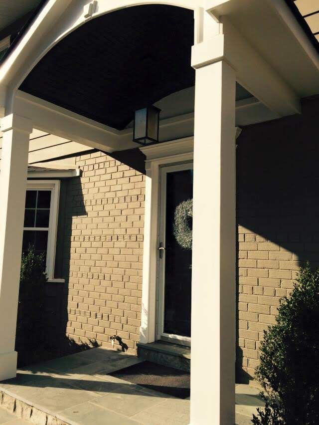 Front porch with white column, arched awning, brick walls, and a glass front door with a wreath