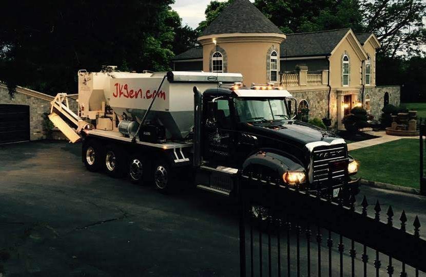 Black dump truck hauling debris in a residential driveway with a large house in the background