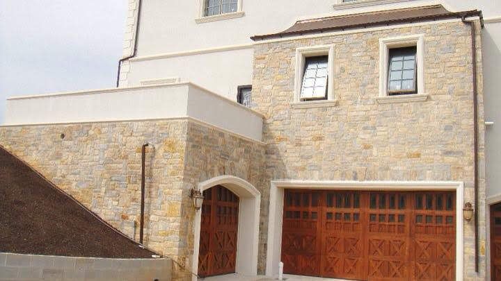Stone house exterior with arched doorway, wooden garage doors, and two small windows