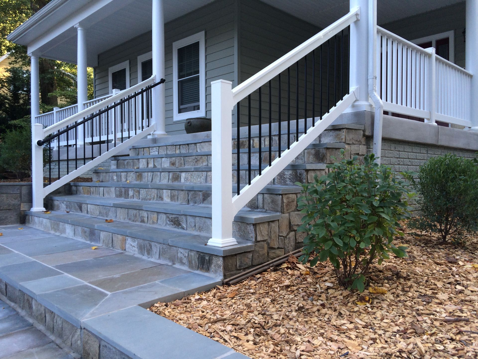 Front steps with gray stone stairs, white railings, and a porch on a house entrance surrounded by mulch.