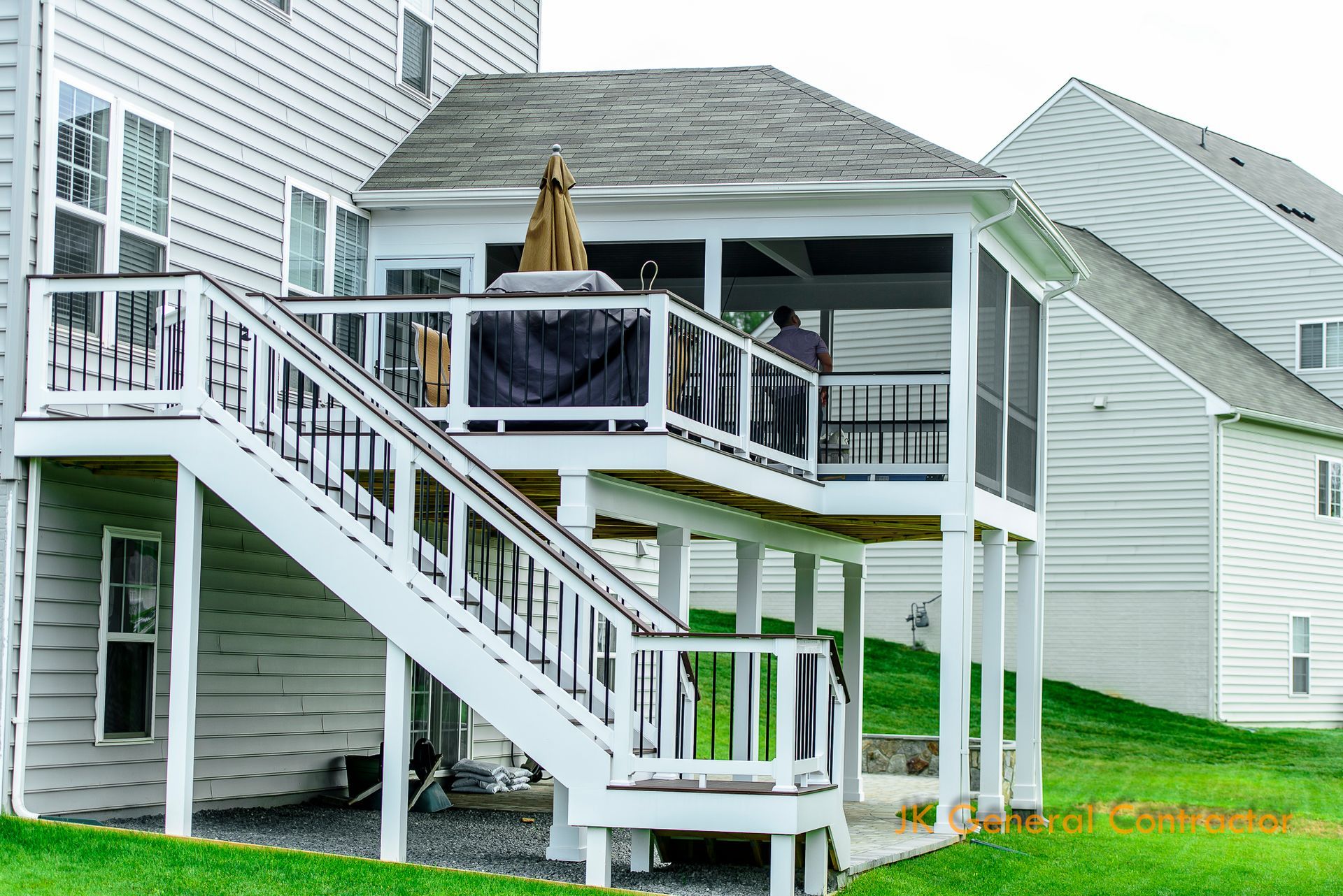 White house with raised wooden deck and stairs overlooking a grassy backyard