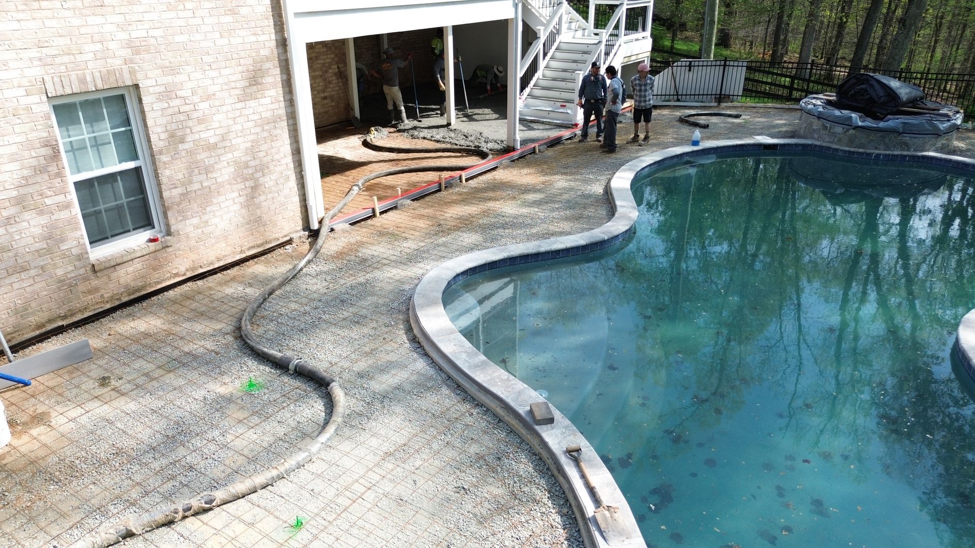 Backyard pool with curved concrete edge beside a house; deck area appears damaged and partially collapsed
