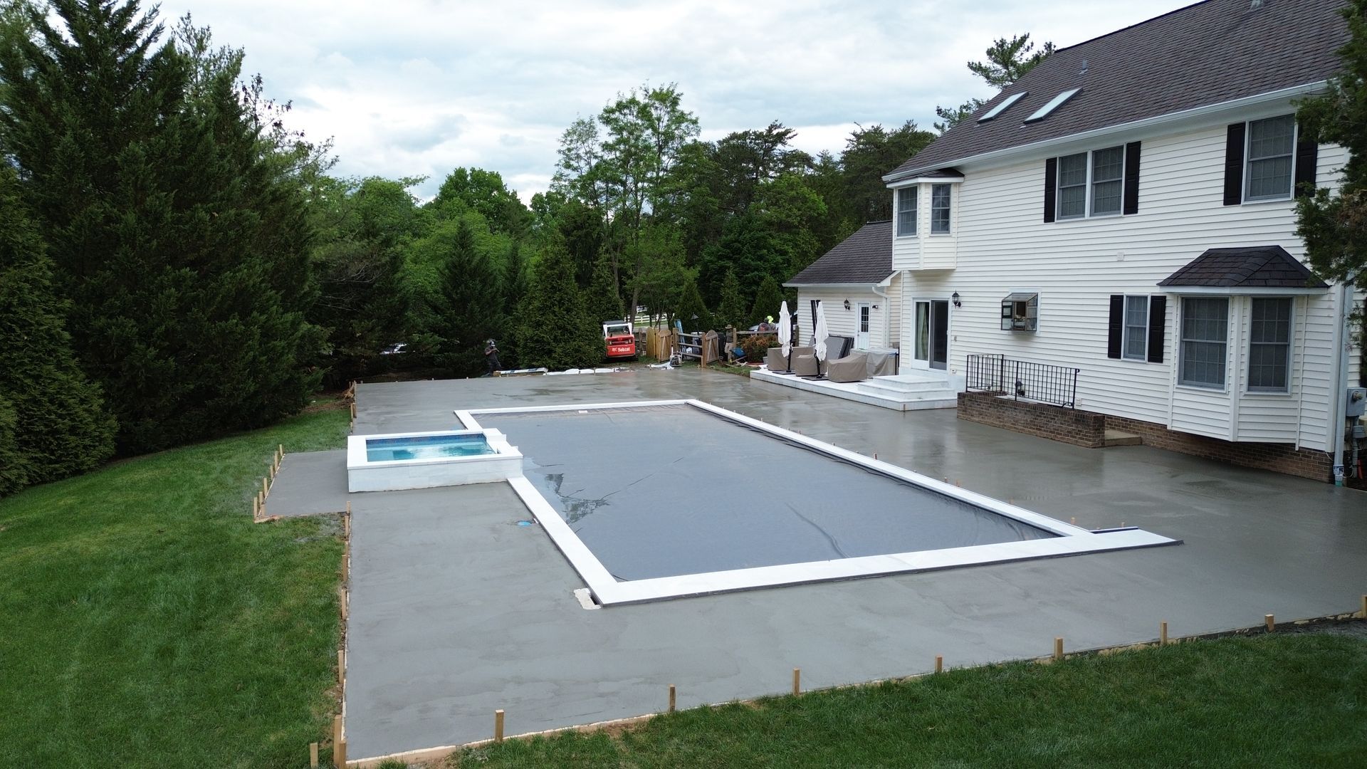 White house beside a rectangular backyard swimming pool with a gray pool cover and patio chairs