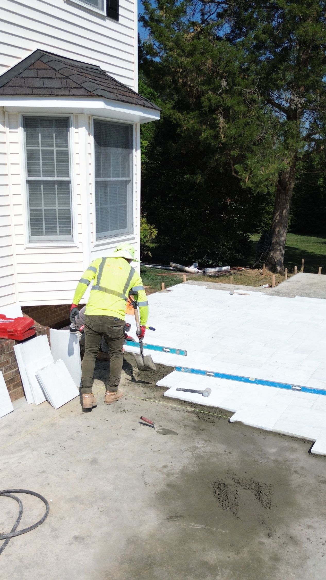 Worker in neon safety vest applying white material beside a house exterior under bright sunlight