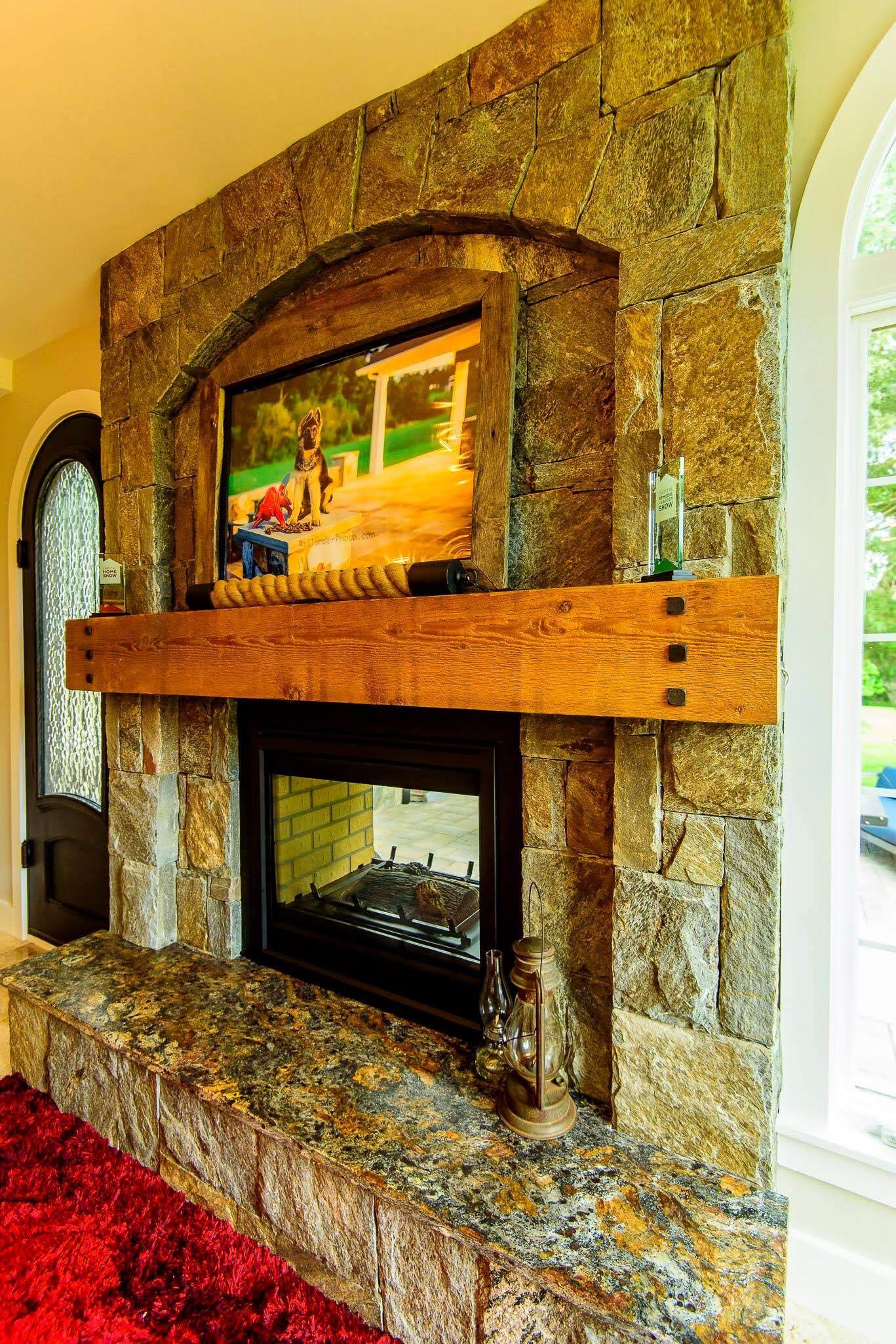 Stone fireplace with arched mirror, wooden mantel, and black insert in a bright room
