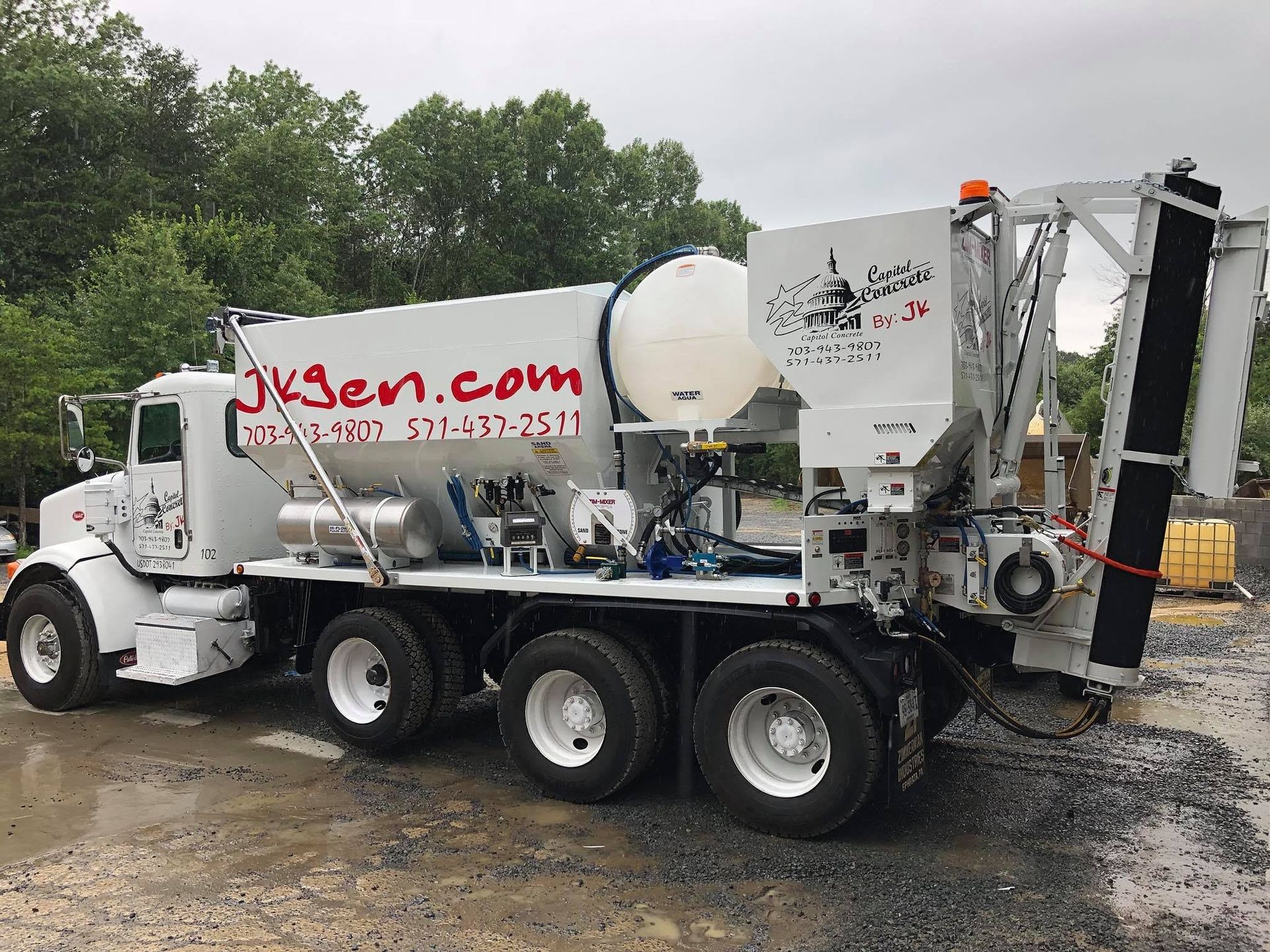 White industrial vacuum truck with tank and hose equipment parked on wet pavement in a tree-lined lot