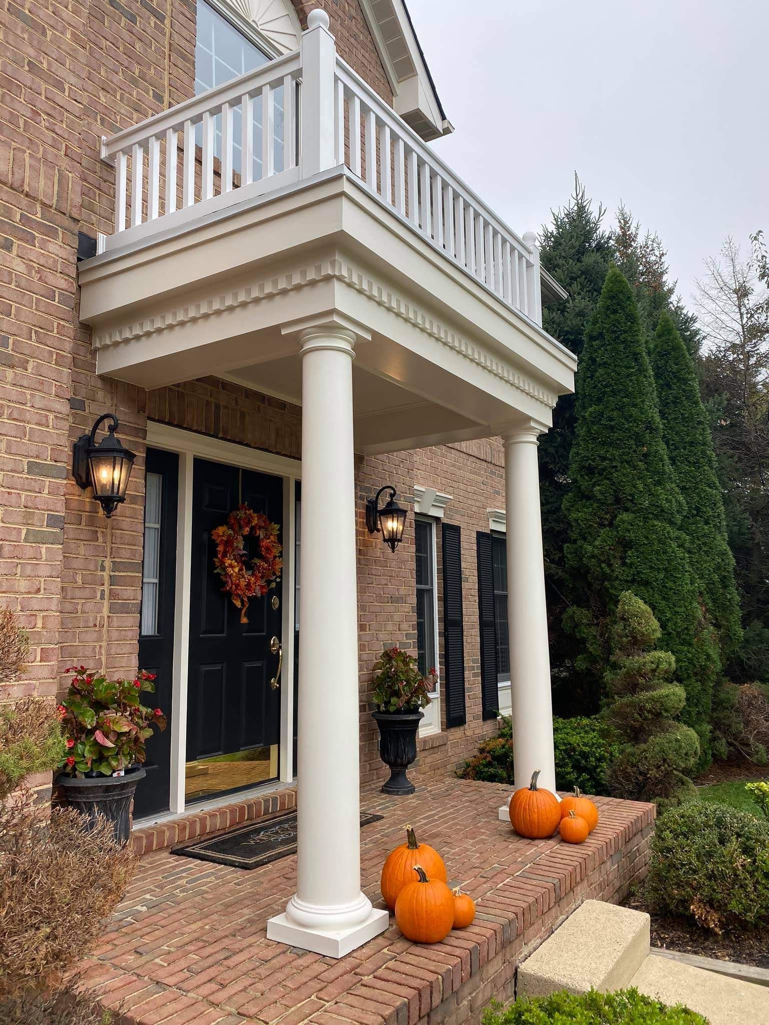 Brick house porch with white columns, pumpkins, and fall wreath by the front door