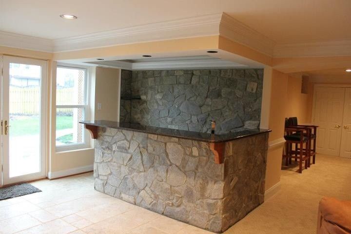 Living room with stone bar and fireplace, beige walls, tiled floor, and large windows on the left