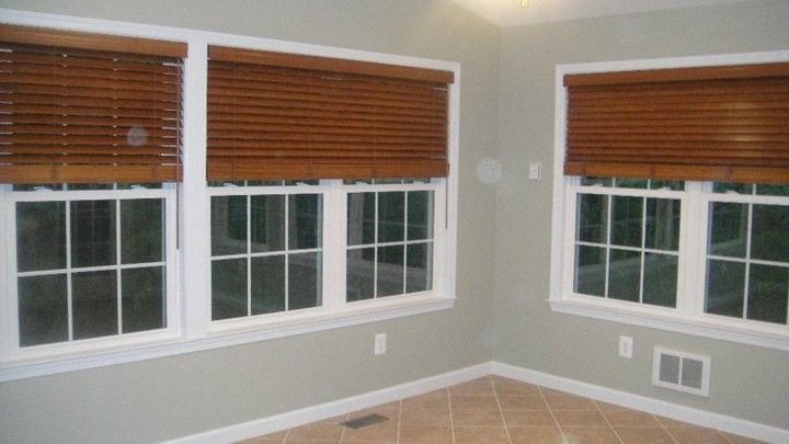 Empty corner room with beige walls, tile floor, and several windows with brown blinds.