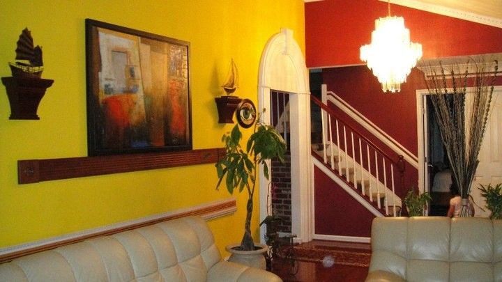 Cozy living room with yellow and red walls, white sofas, staircase, artwork, and hanging light fixture