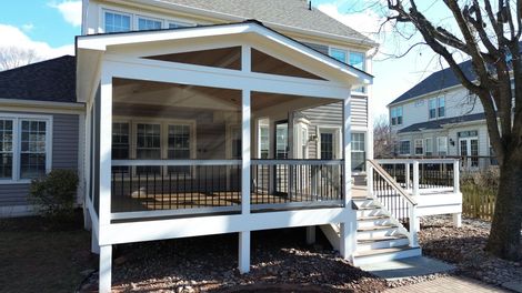 Covered porch with screened railings, green trees outside, and a ceiling fan overhead
