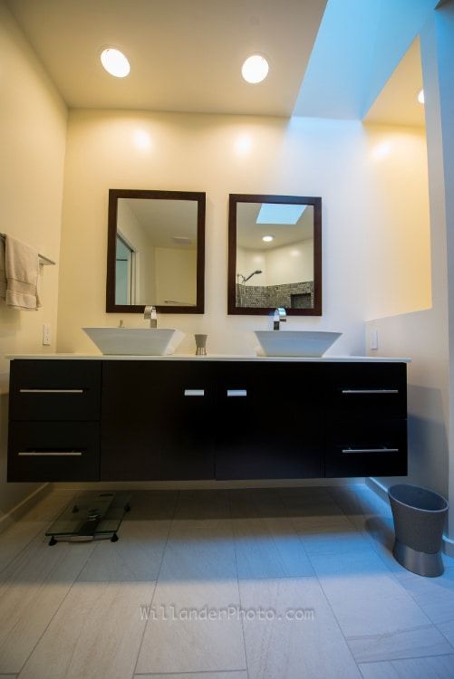 Modern bathroom vanity with two mirrors, black cabinets, and warm ceiling lights