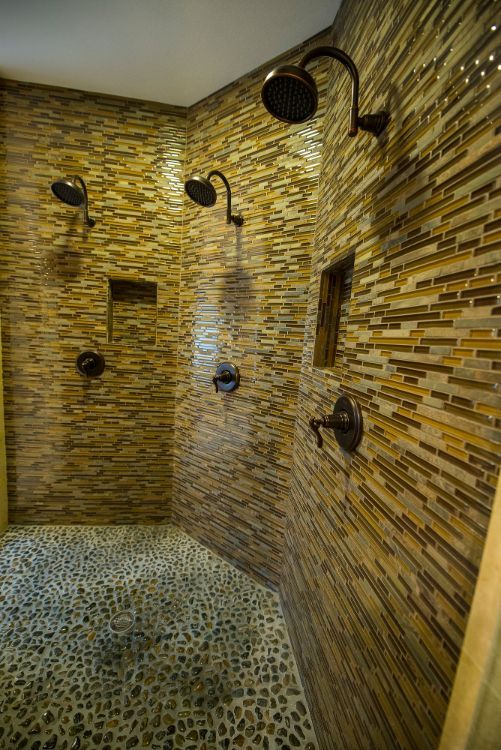 Stone-tiled walk-in shower with multiple showerheads and a pebble floor