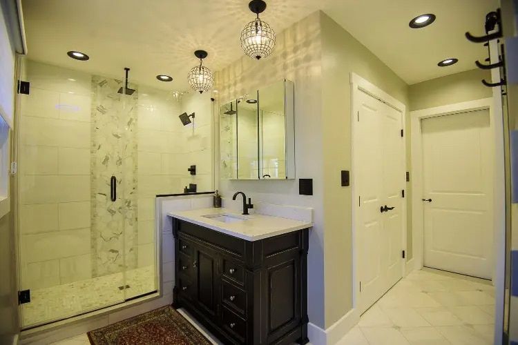 Modern bathroom with glass shower, dark vanity, large mirror, and white tile flooring.