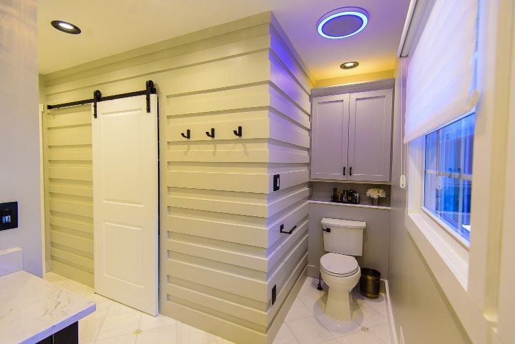 Small bright bathroom with white shiplap walls, black hooks, a toilet, sink, and window.