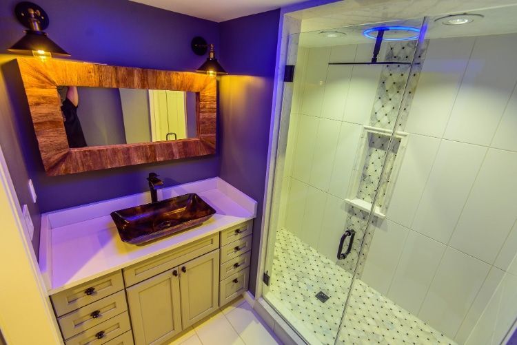 Modern bathroom with vanity, large mirror, and glass shower under warm purple lighting