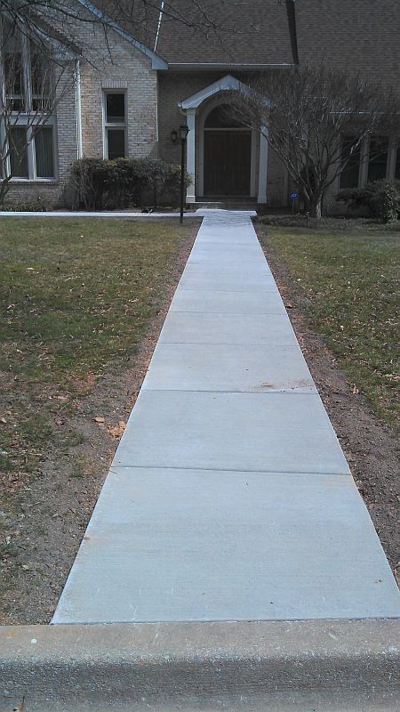 Concrete walkway leading to a house entrance with an arched doorway and lawn on both sides