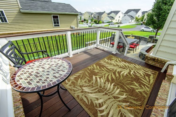 Wooden backyard deck with mosaic table, patterned rug, railing, and suburban houses beyond