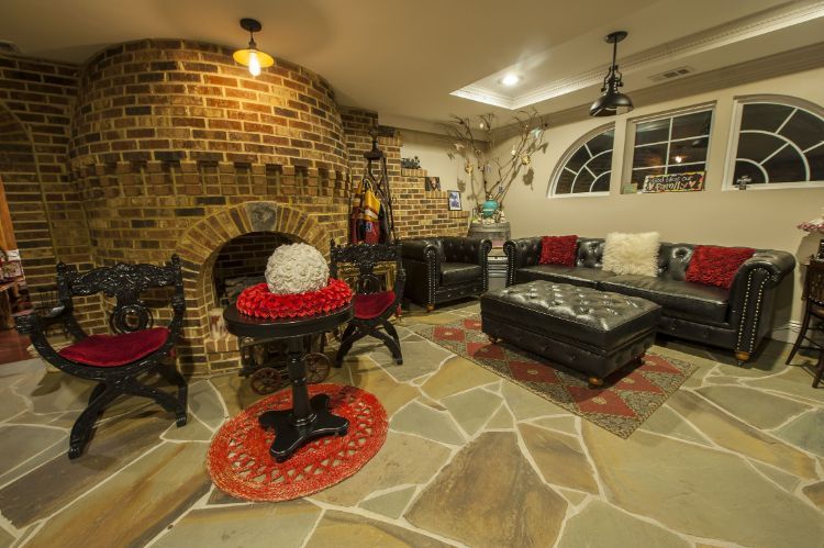 Brick patio with black wicker seating, red cushions, and a stone fire pit under warm lighting