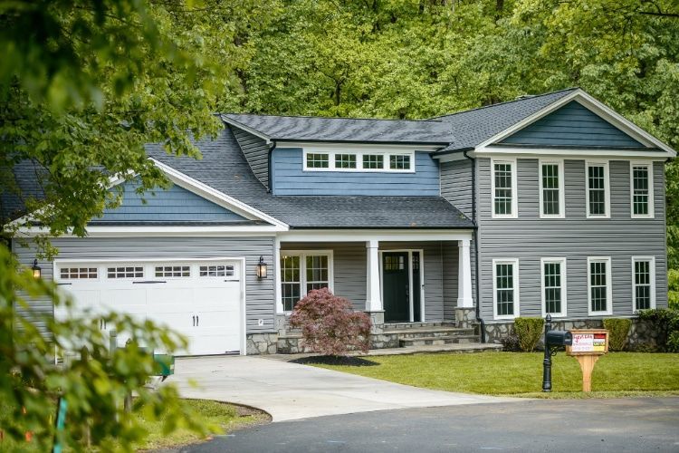 Suburban gray house with garage, front porch, and trees surrounding the yard