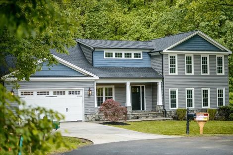 Gray suburban house with white trim, a two-car garage, and a front porch surrounded by trees.