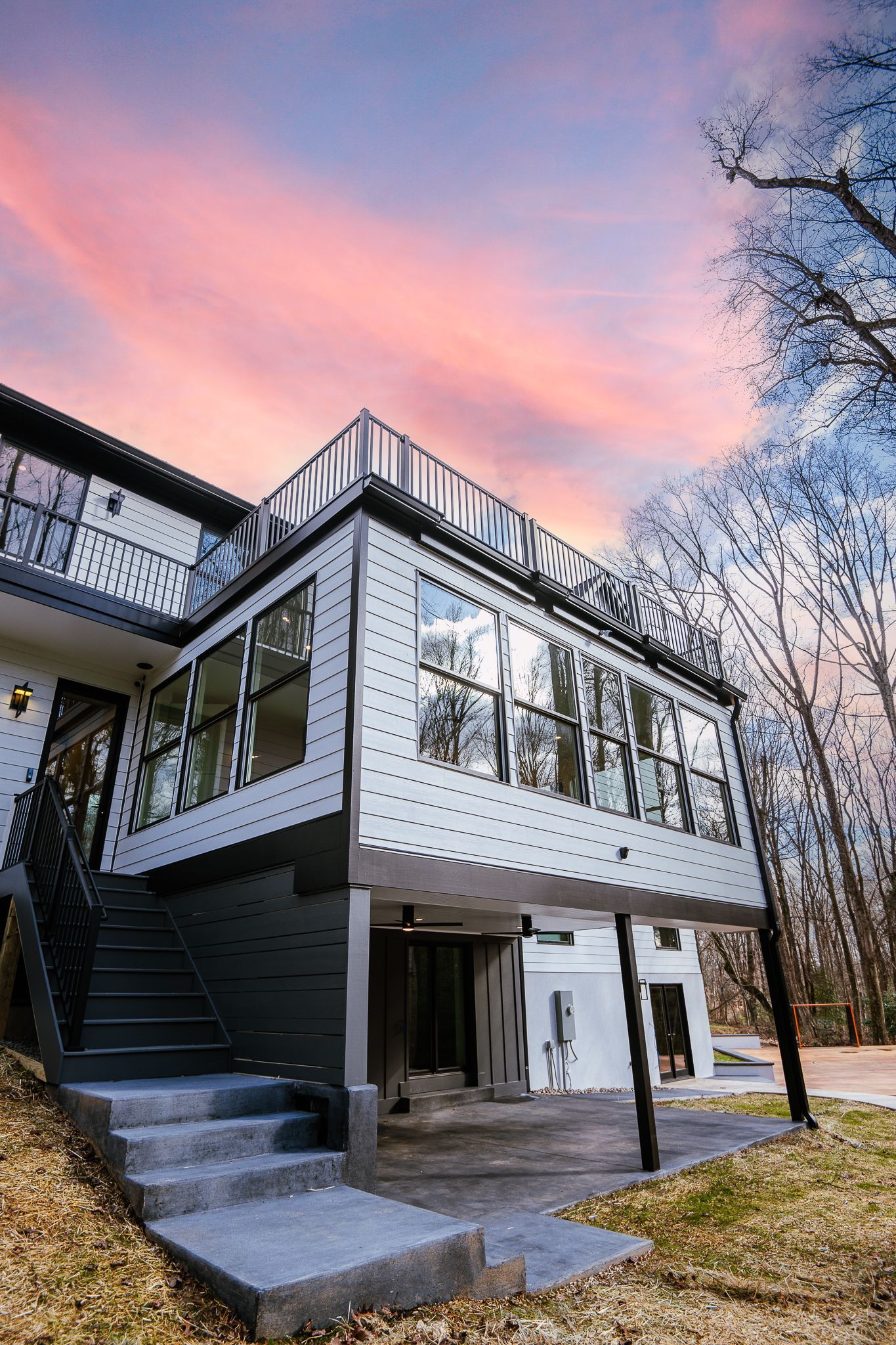 Modern two-story house with white siding, black stairs, and a pink sunset sky