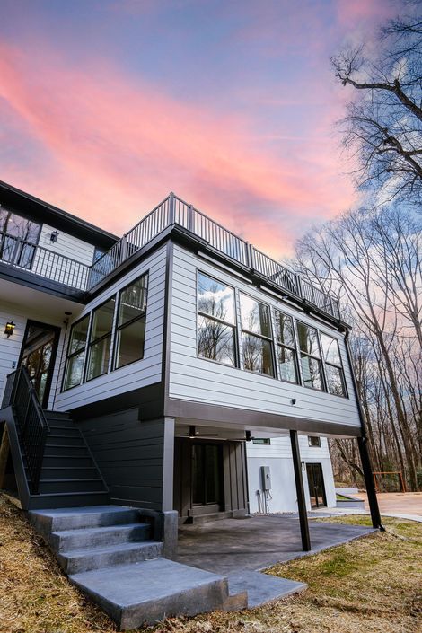 Gray suburban house with white trim, a two-car garage, and a front porch surrounded by trees.